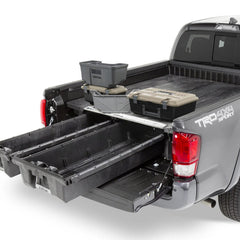 Open DECKED drawer system installed in a Toyota Tacoma bed with storage cases on a light background