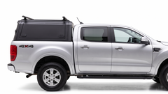 Silver Ford Ranger with a black IRONHAUL aluminum truck canopy and roof crossbars, shown from the passenger-side profile