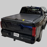 Black hard retractable tonneau cover installed on a pickup truck with a light neutral background