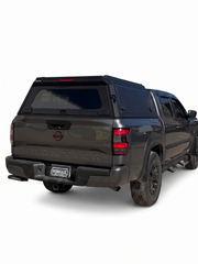 Grey Nissan Frontier with a black IRONHAUL aluminum truck canopy, shown from a vertical rear three-quarter view.