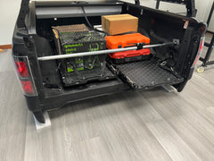 IRONHAUL ratcheting cargo bar installed across a pickup bed to stabilize tools and boxes