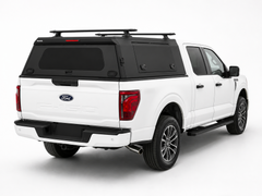 Rear three-quarter view of a white Ford F-150 with an IRONHAUL aluminum truck canopy, side access door, rear window, and roof cross bars
