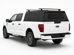 Rear left-side view of a white Ford F-150 with an IRONHAUL aluminum truck canopy, side access door, rear window, and roof cross bars