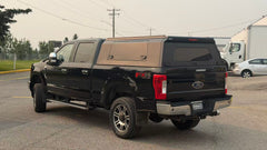 Side and rear view of a black Ford Super Duty with an installed IRONHAUL aluminum truck canopy, side access door, and rear window