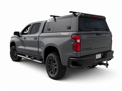 Grey Chevrolet Silverado with a black IRONHAUL aluminum truck canopy and roof crossbars, shown from the rear-left angle.