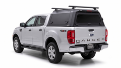 Silver Ford Ranger with a black IRONHAUL aluminum truck canopy and roof crossbars, shown from the rear-right angle