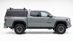 Side view of a silver Toyota Tacoma with an IRONHAUL aluminum truck canopy V2, side access door, and roof cross bars