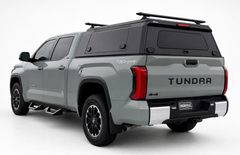 Rear three-quarter view of a grey Toyota Tundra with an IRONHAUL aluminum truck canopy V2, rear window, side access door, and roof cross bars
